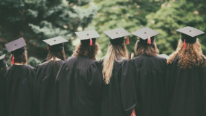 A photo of a group of graduated students back view standing outside between trees.