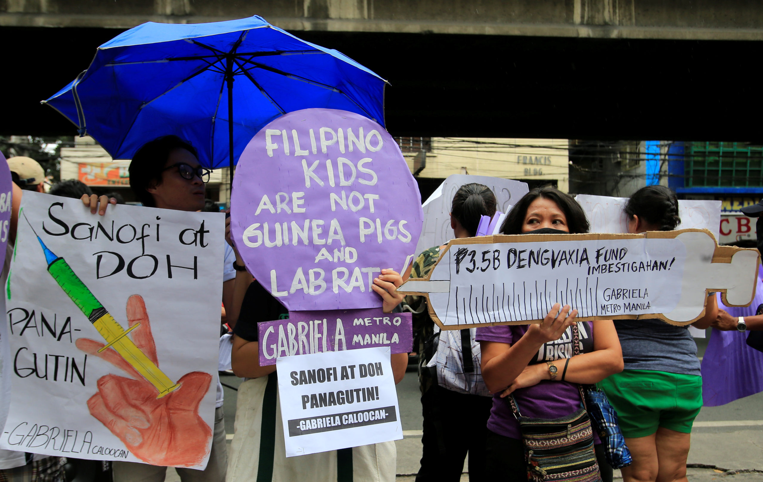 People display signs and a mock syringe, with the phrase "3.5 billion pesos Dengvaxia fund investigate" featured on it, during a protest in front of the Philippine Department of Health (DOH) in metro Manila, Philippines December 5, 2017. The poster (L) reads: "Sanofi and DOH should be held accountable". REUTERS/Romeo Ranoco