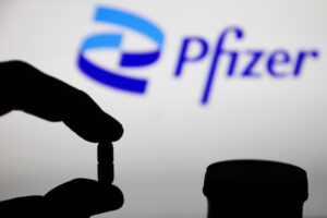 Medicine pills are seen with Pfizer logo displayed on a screen in the background in this illustration photo