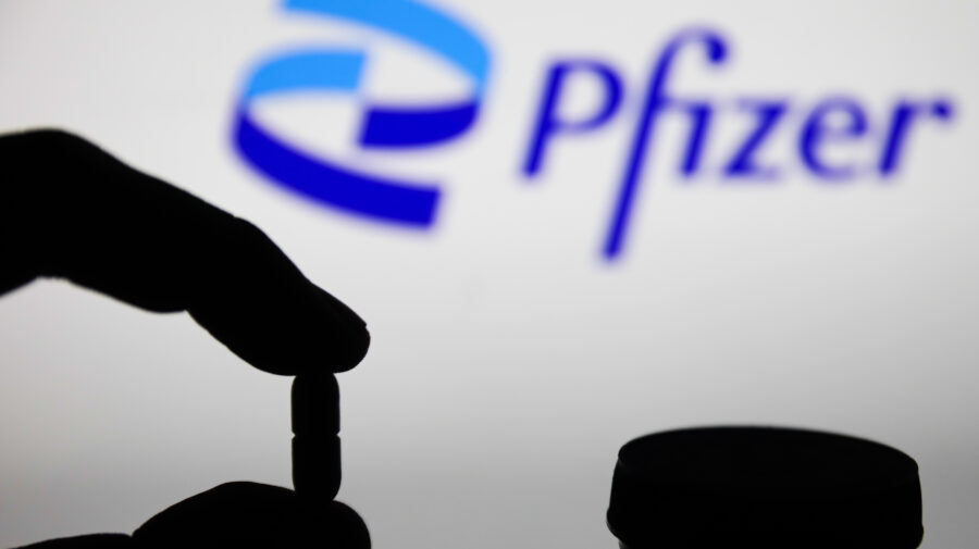Medicine pills are seen with Pfizer logo displayed on a screen in the background in this illustration photo